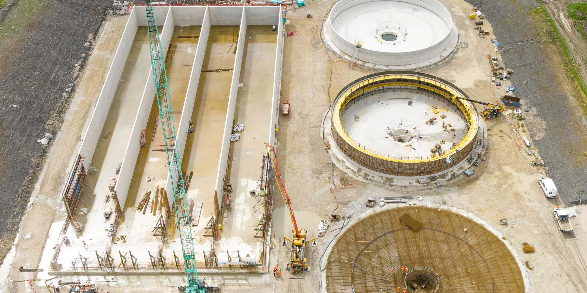 Aerial view of multiple in situ poured concrete tanks at different construction stages on a Tank Consult project, including rectangular settlement lanes and circular tank bases with formwork, cranes and site equipment.