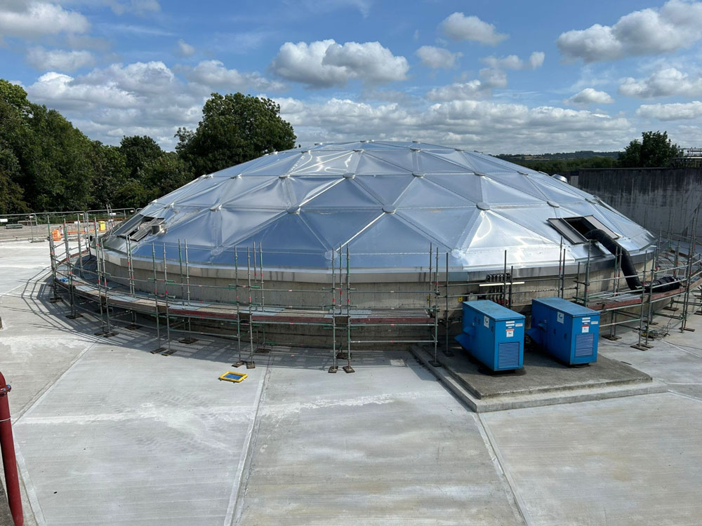 Aluminium geodesic domed roof installed on a concrete tank, surrounded by scaffolding and site equipment on a wastewater treatment site.