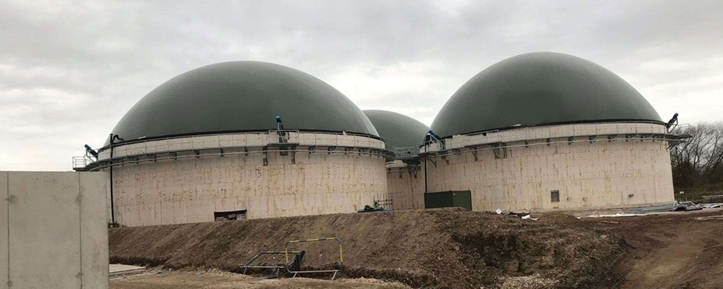 Three large anaerobic biogas digestion tanks with dome roofs under construction on a prepared site.